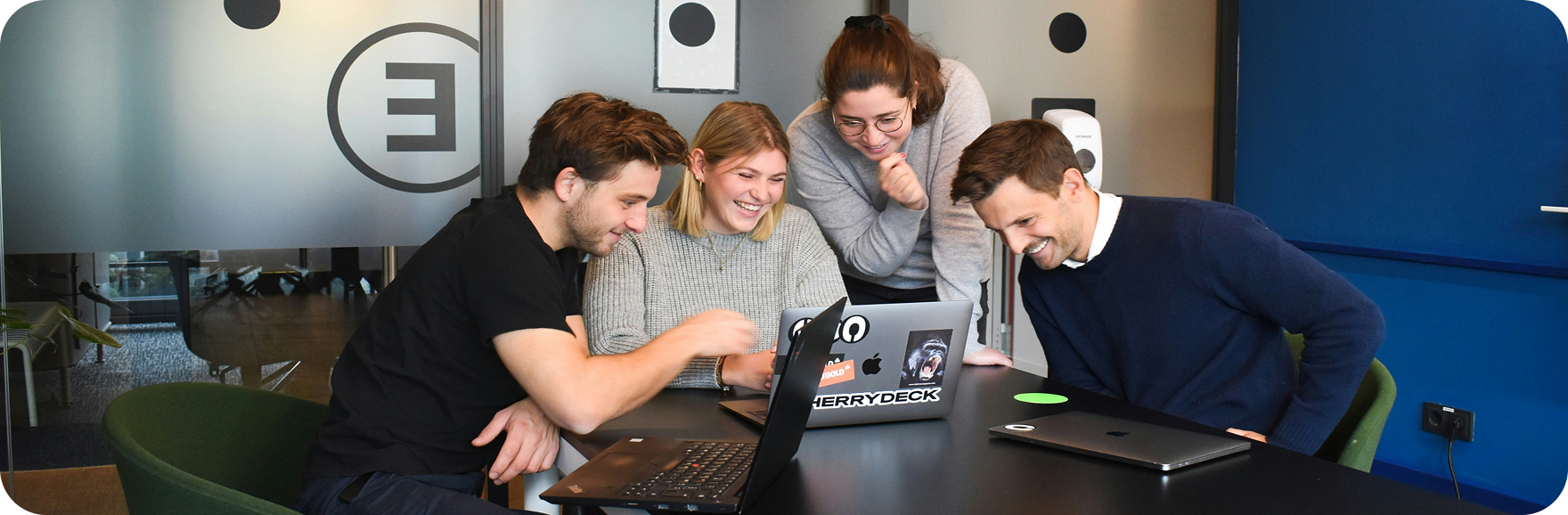 Team photo with five diverse team members sitting together with laptops surrounded by plants